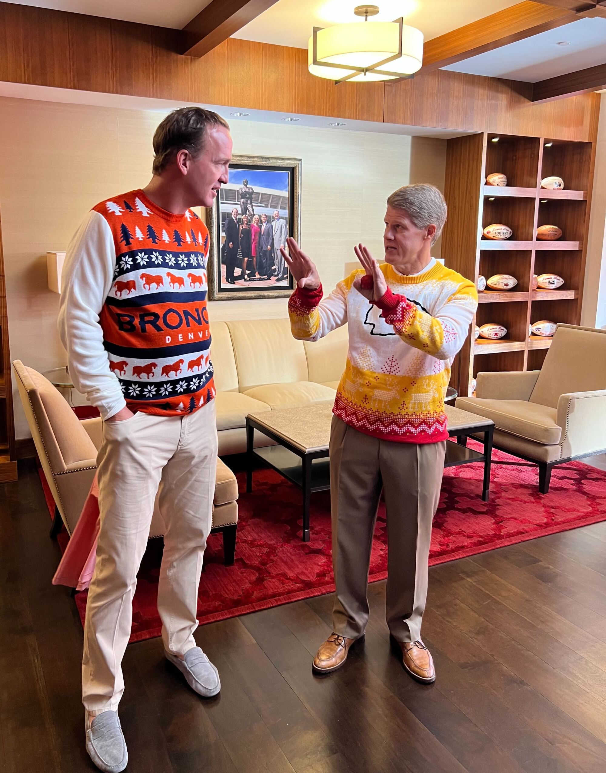 Clark Hunt talks to Peyton Manning, both in ugly Christmas sweaters, during a filming inside the in-stadium apartment.