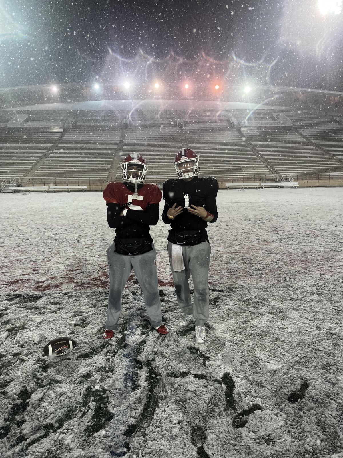 Two football players stand on a football field covered in snow at night.