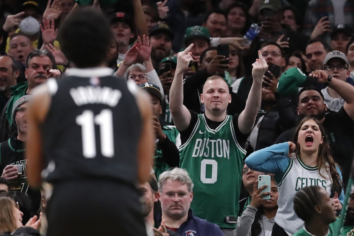 EDS NOTE: OBSCENITY - A fan gestures and others yell as Brooklyn Nets' Kyrie Irving (11) takes a free throw during the second half of Game 2 of an NBA basketball first-round Eastern Conference playoff series against the Boston Celtics, Wednesday, April 20, 2022, in Boston. (AP Photo/Michael Dwyer)
