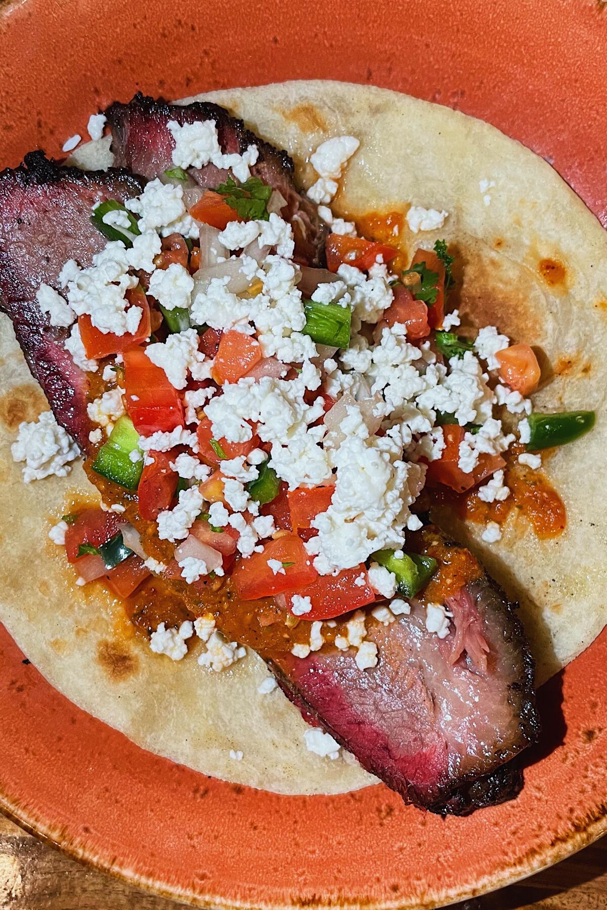An overhead, vertical closeup of a brisket taco, served on a flour tortilla and topped with cheese and pico de gallo.