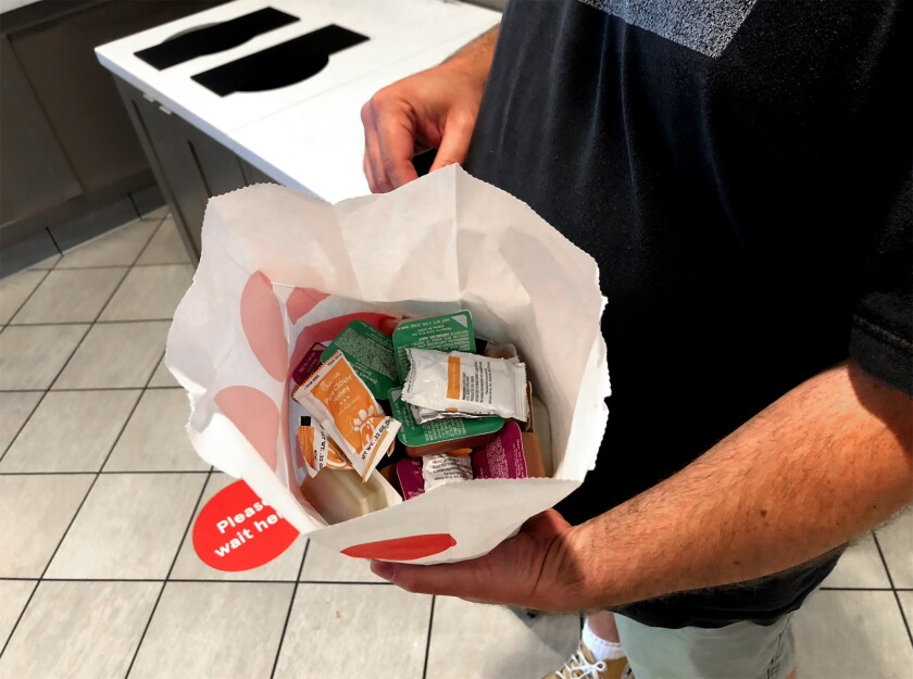 A man holds packets of various sauces. 