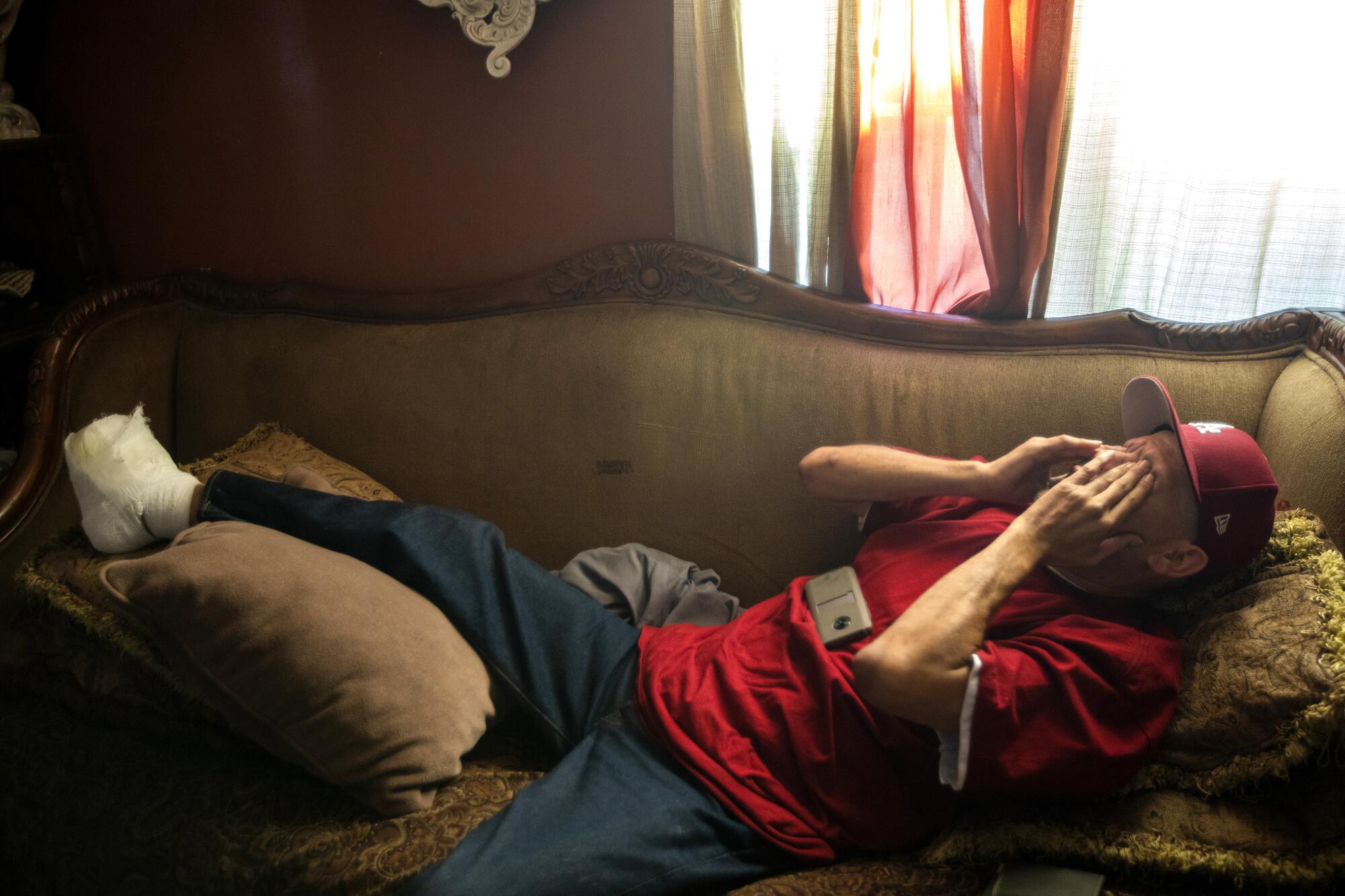 Tony Zamora, recovering from having all the toes on his right foot removed, rubs his eyes as he lies on his mother's sofa.