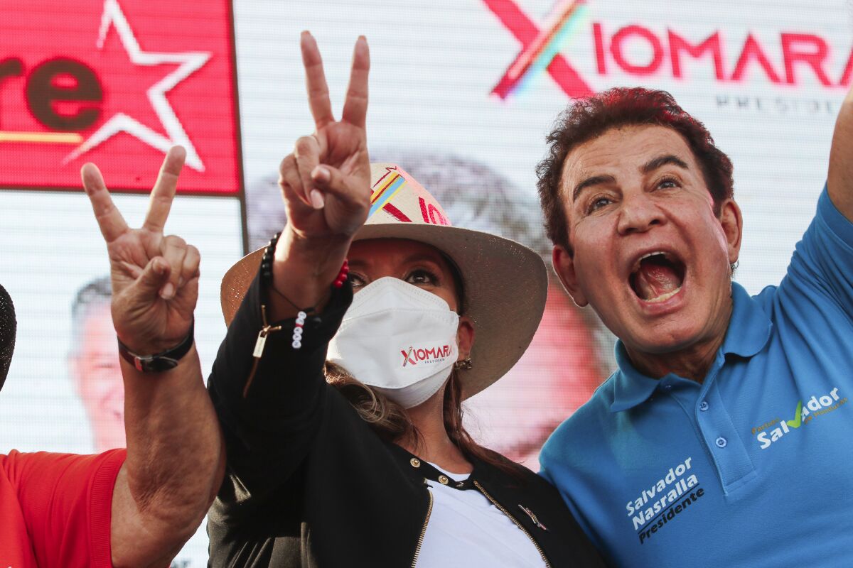 A masked woman in a hat, center, gives the peace sign. Next to her is a man in a blue shirt with the words Salvador Nasralla