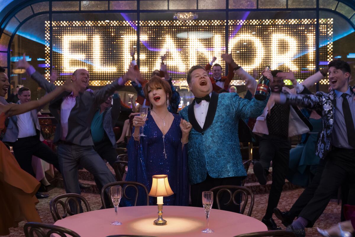 A movie still shows Meryl Streep and James Corden clutching Champagne and singing