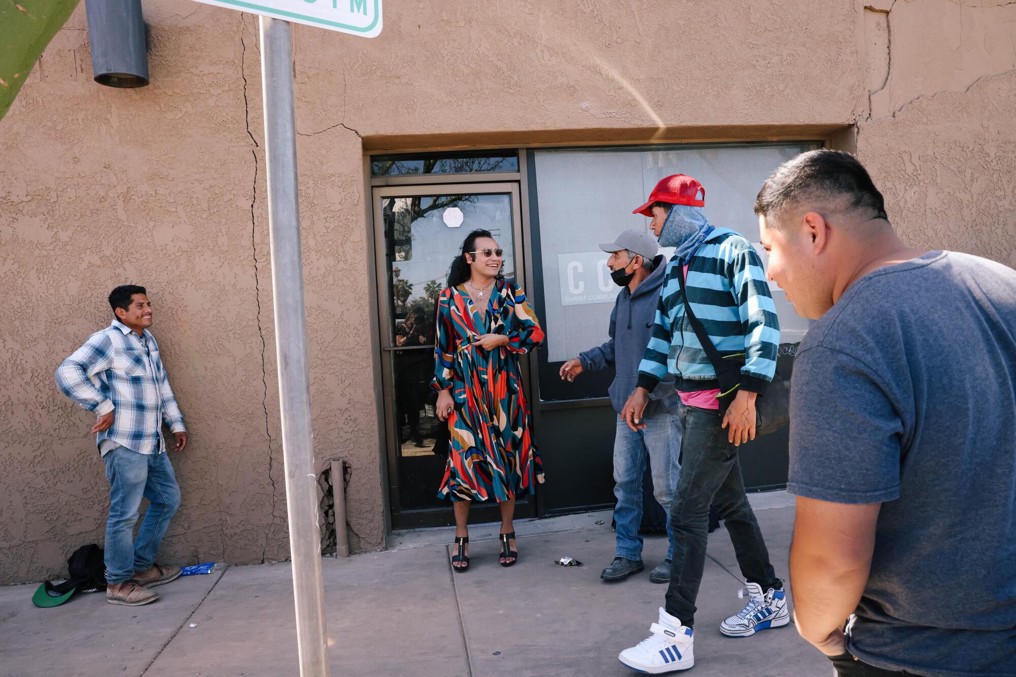 A person in a colorful dress greets passing farmworkers on a Calexico sidewalk. 