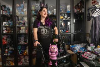 Northridge, CA - July 23: Disney fan Rosie Keiser, 55, stands for a portrait among curios in her Northridge home. Keiser who suffers from multiple sclerosis uses a walker to traverse the park. Keiser recently received a Disneyland Disability Access Service Pass, which allows her to wait for rides outside of the usually long standby lines. on Tuesday, July 23, 2024 in Northridge, CA. (Brian van der Brug / Los Angeles Times)