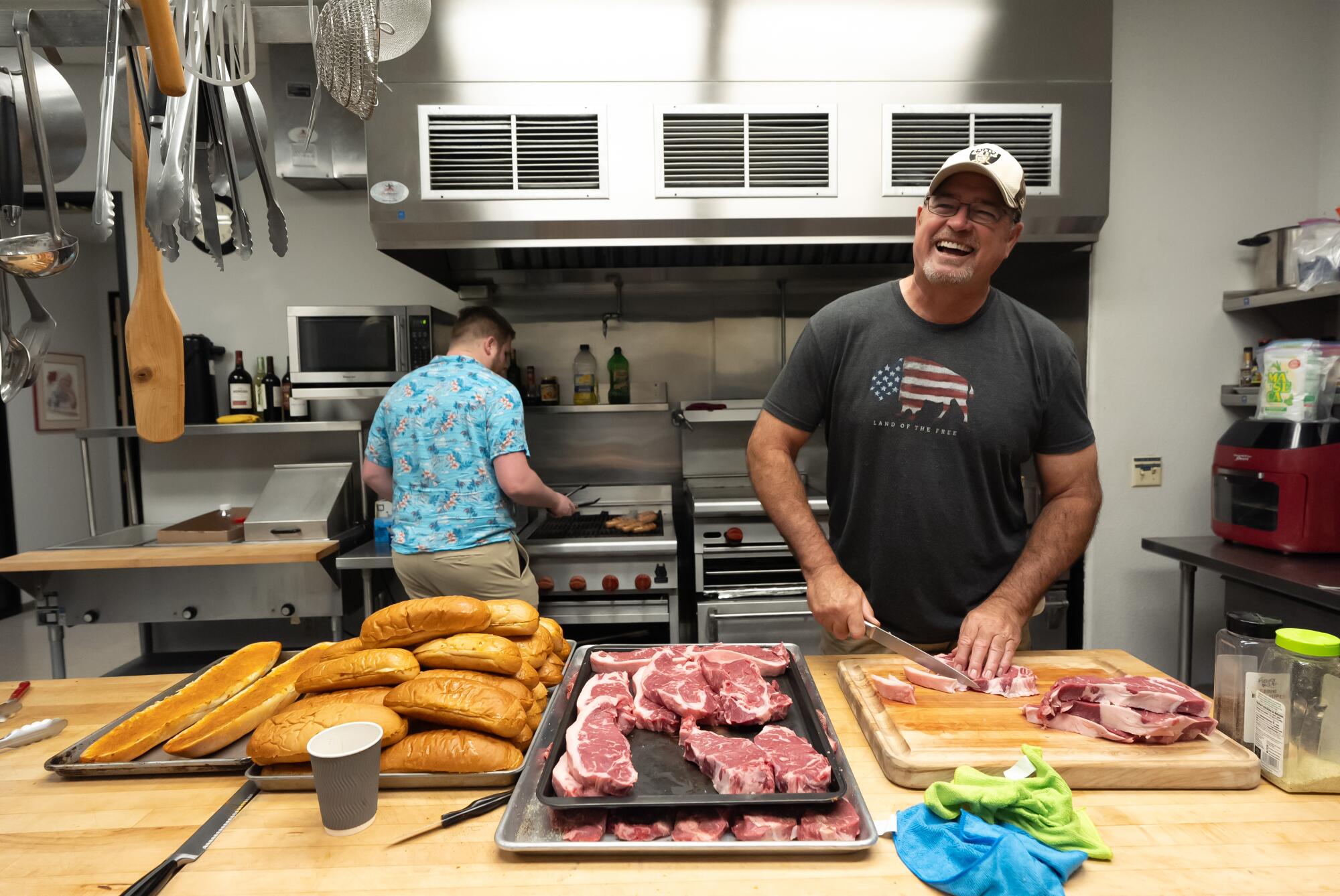 A man and a boy in a large kitchen with piles of bread and meat.