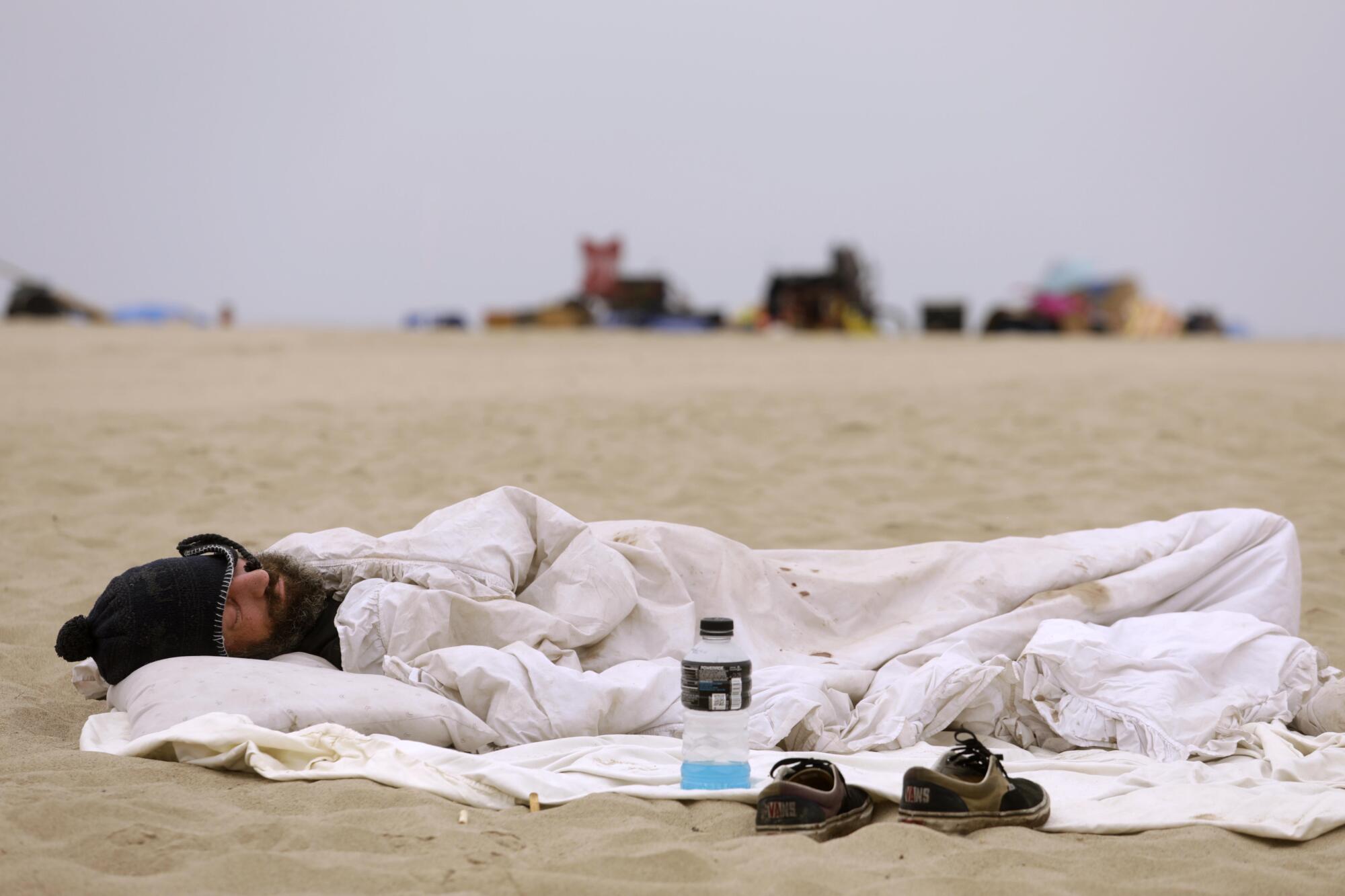 A homeless man sleeps on the beach before City of Los Angeles sanitation workers showed up to clear homeless encampments