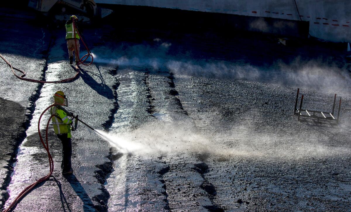 Workers use water and compressed air to remove loose rocks between the upper and lower chute in preparation for a layer of enriched roller-compacted concrete at the Lake Oroville flood control spillway on Oct. 25,