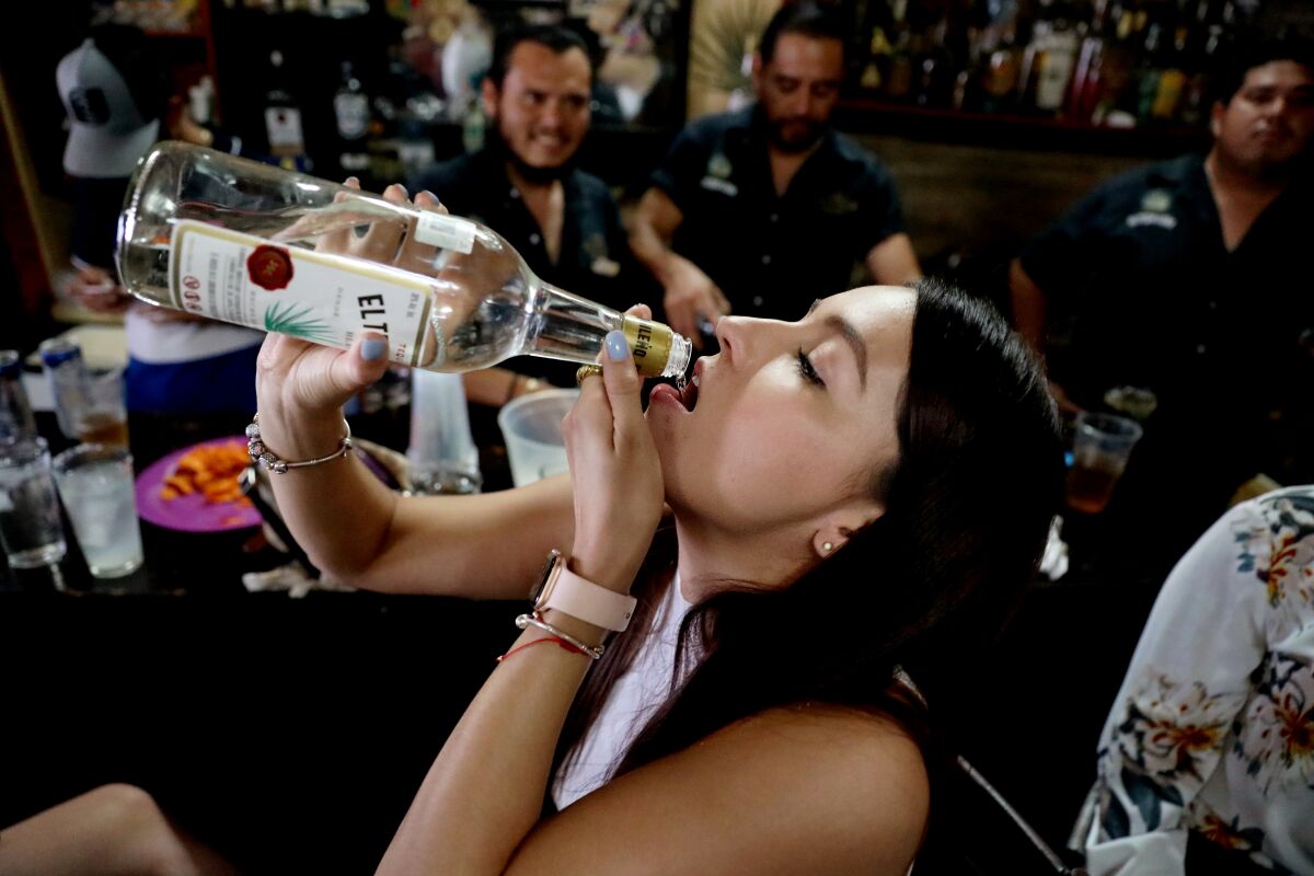 A woman drinks from a bottle of tequila.