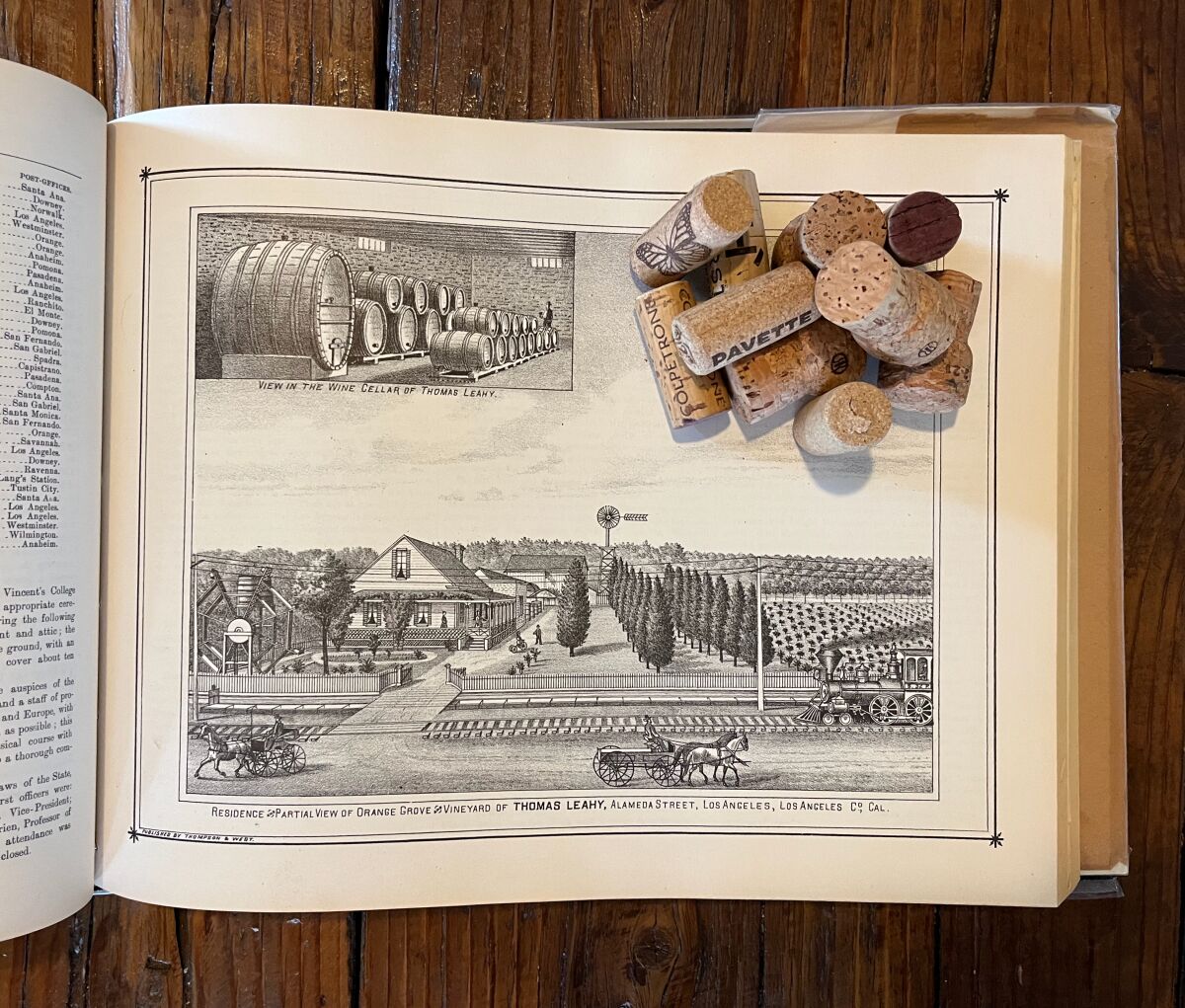An open book shows black and white images of wine barrels and a farm, wine bottle corks are arranged on the page