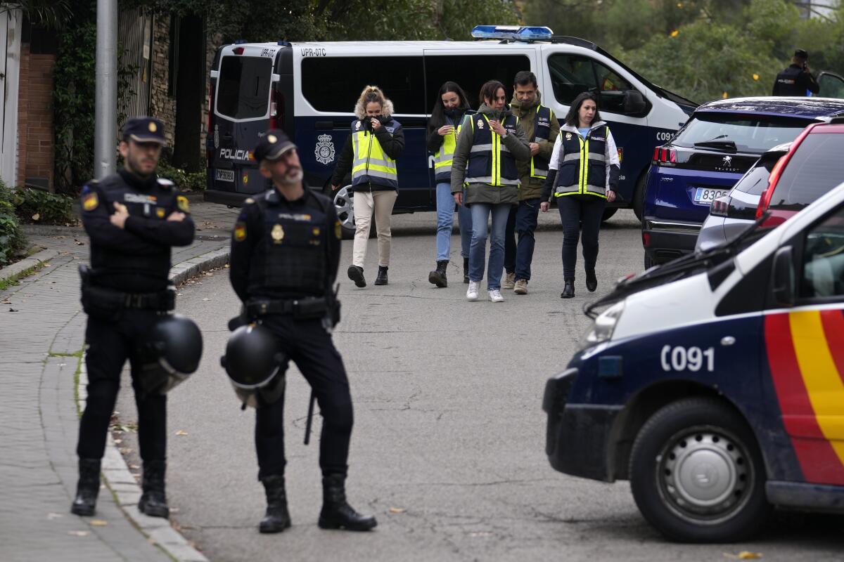 Police officers stand guard as other officers in yellow vests walk back at the cordoned off area next to the Ukrainian embassy in Madrid, Spain, Wednesday, Nov. 30, 2022. Spain's Interior Ministry says police are investigating reports of a blast at the Ukrainian embassy in Madrid. The ministry says police were told an employee at the embassy was slightly injured handling a letter in what it described as "a deflagration." (AP Photo/Paul White)