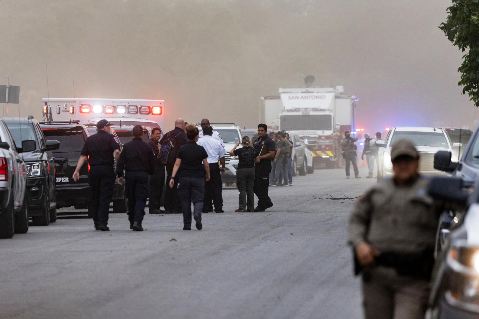 Law enforcement personnel are seen near long lines of emergency vehicles against a cloudy background