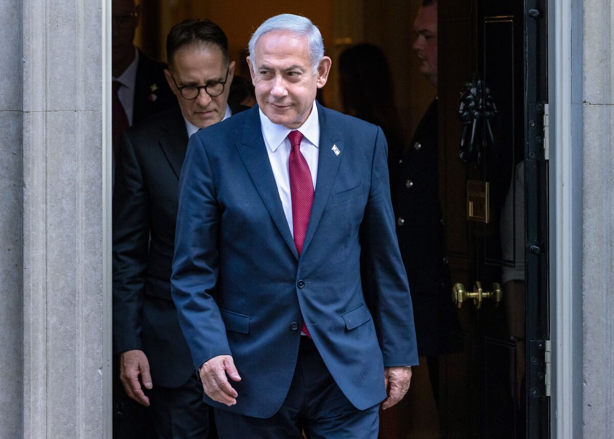 Benjamin Netanyahu walks out of a doorway, slightly smiling. 