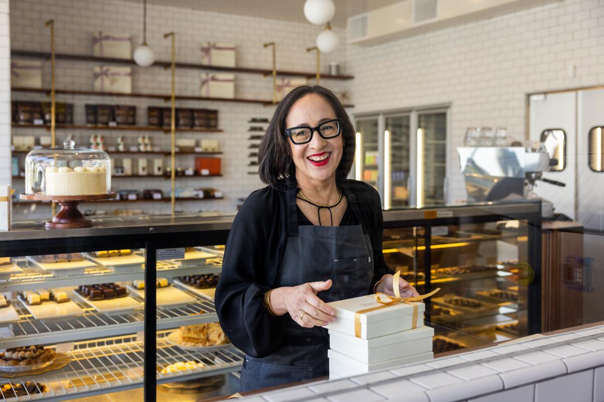 Valerie Gordon with stacked boxes in front of her and trays of baked goods behind her in her store.