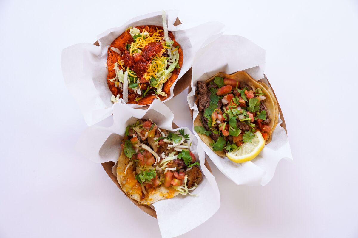 Three tacos rest on paper inside cartons.