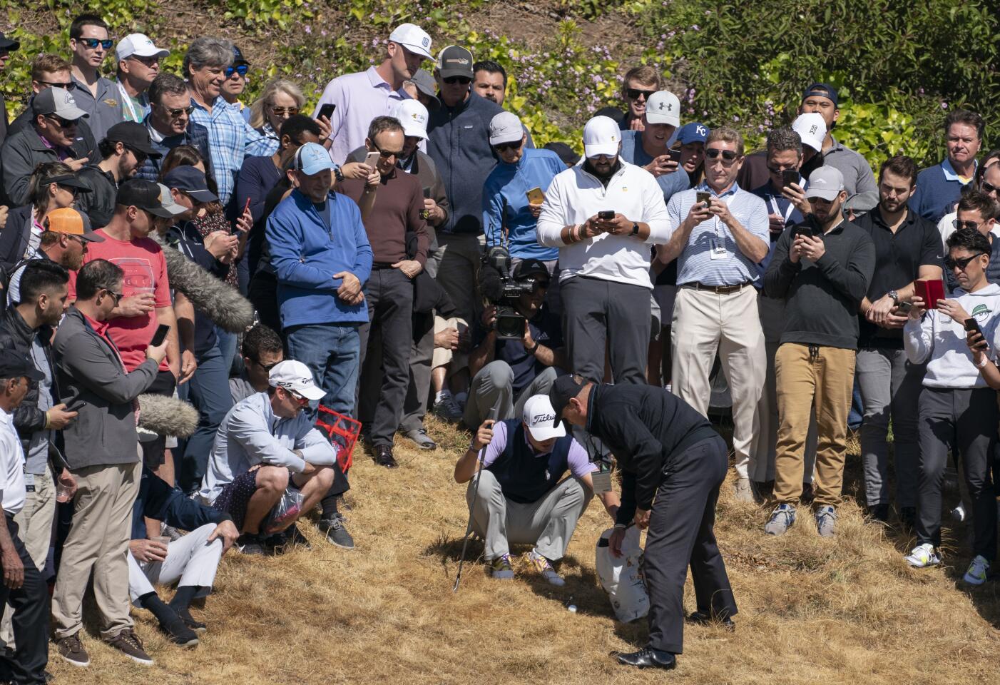 Justin Thomas gets a ruling from an official after his golf ball landed in a woman's shopping bag in the rough near the second green during the first round of the Genesis Invitational at Riviera Country Club on Feb. 13, 2020.