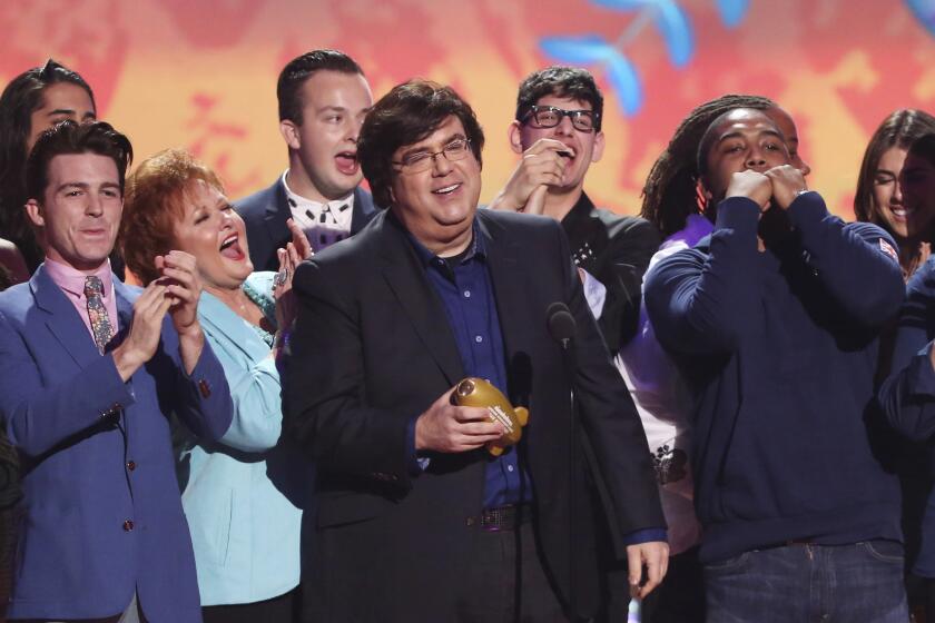 A man holding an award onstage while a group of people cheer around him