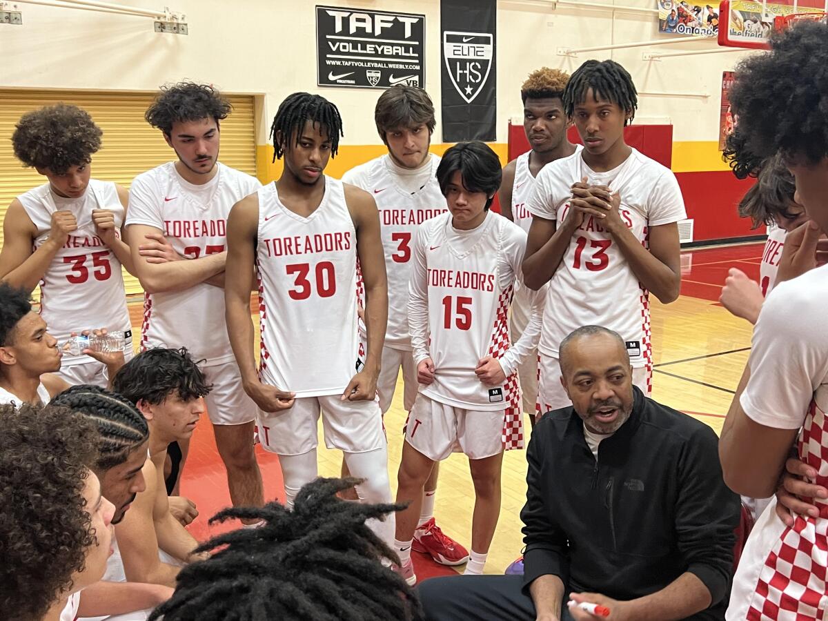 Taft coach Derrick Taylor speaking to his team in a sideline huddle during a playoff game