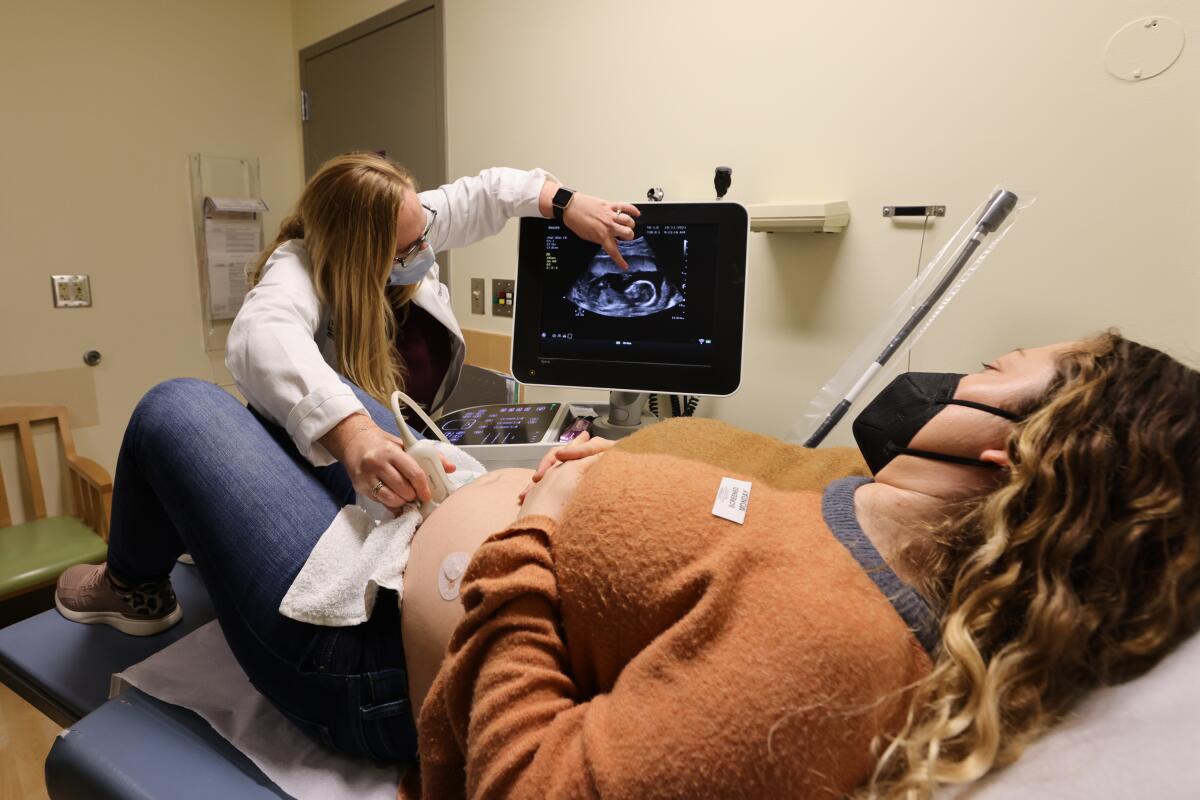 A woman reclines on a table as another woman points to an image on a screen.  