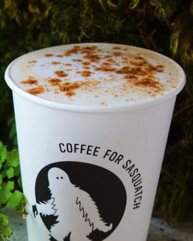 A white to-go cup sprinkled with orange spices. The side reads Coffee for Sasquatch.