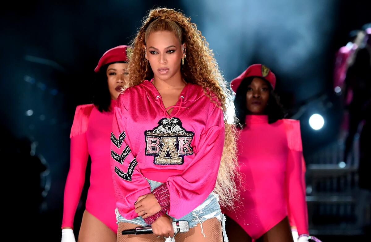 Beyoncé, in a pink sweatshirt embellished with “ΒΔΚ” and denim cut-offs, performs on stage at Coachella. 