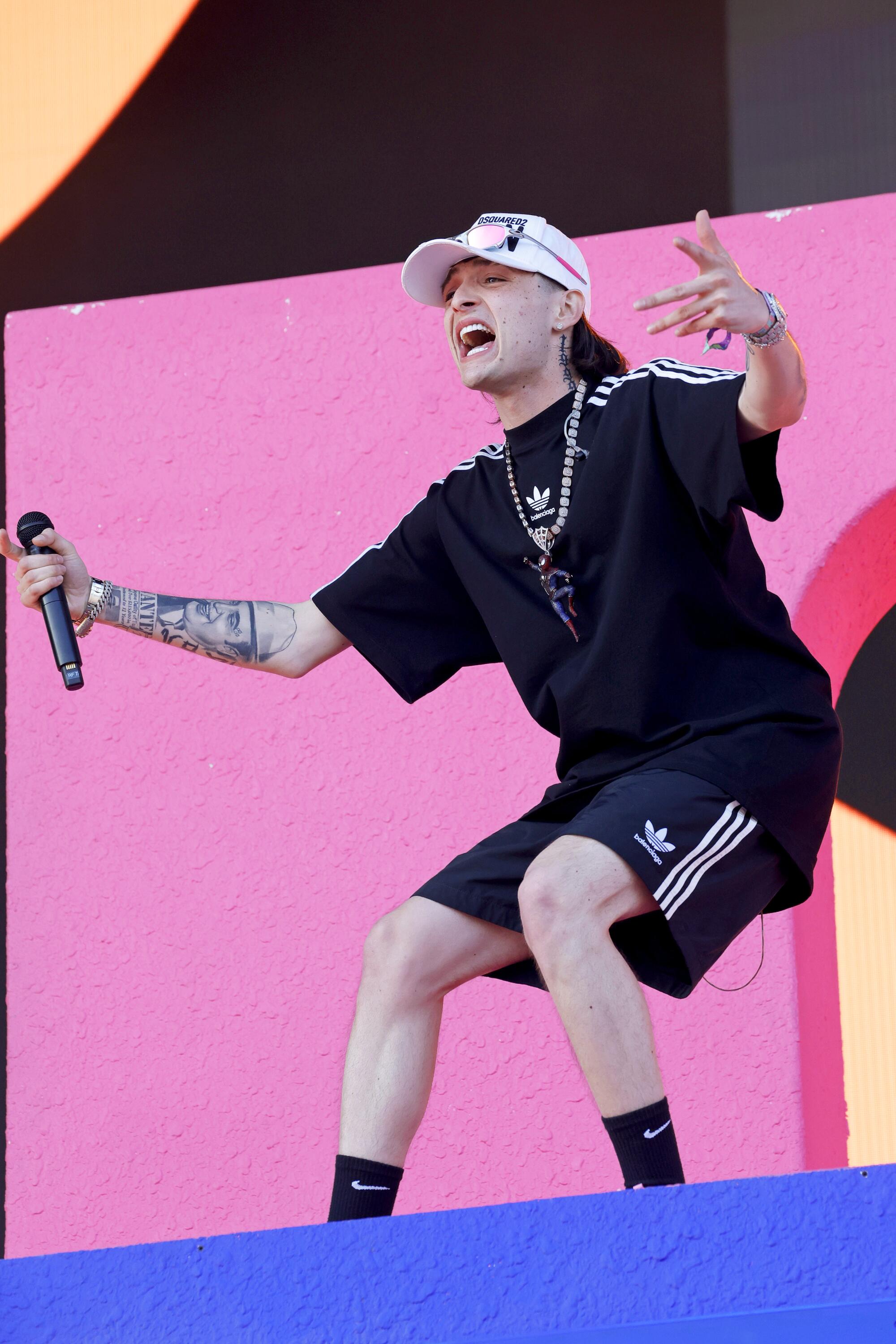 A Latin singer in black shorts and black T-shirt performing onstage and exhorting the crowd