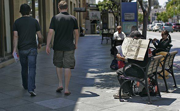 A man holds a sign asking for donations while sitting on a public bench on Santa Monica Boulevard at the Third Street Promenade in Santa Monica. The city has voted to prohibit panhandling from public seats and benches along the promenade and in the transit mall area, which runs along Broadway and Santa Monica boulevards.