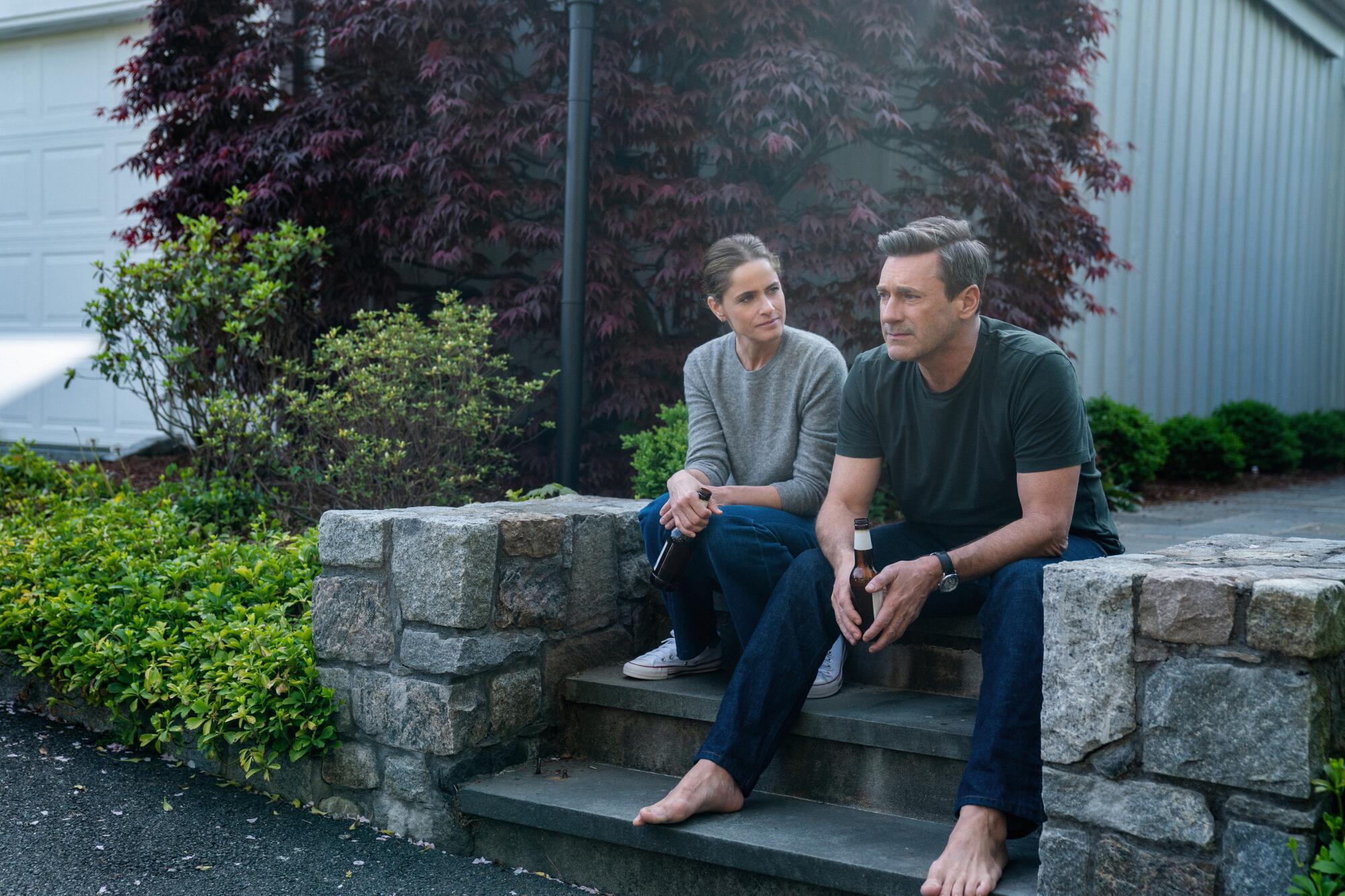 Amanda Peet and Jon Hamm sit on the stone steps of a home.