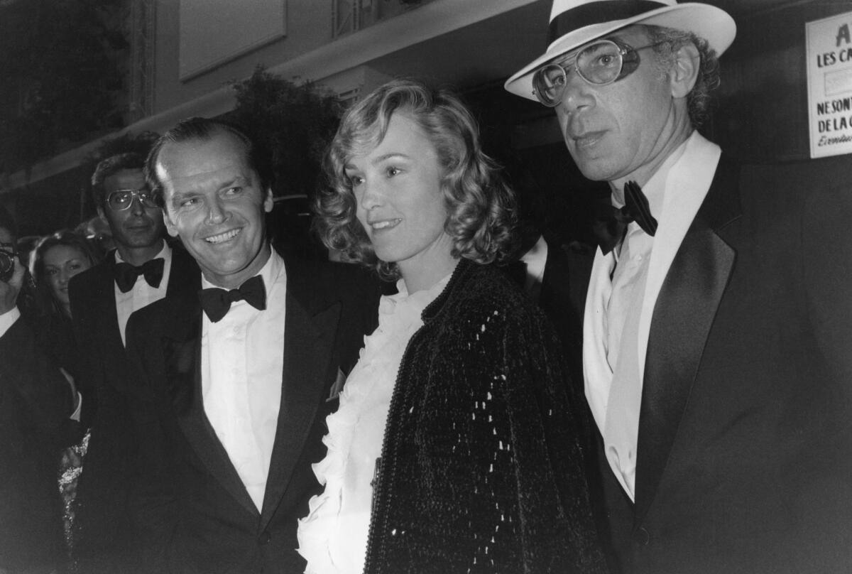 A black-and-white image of a woman in a ruffled white shirt standing between two men in tuxedos.