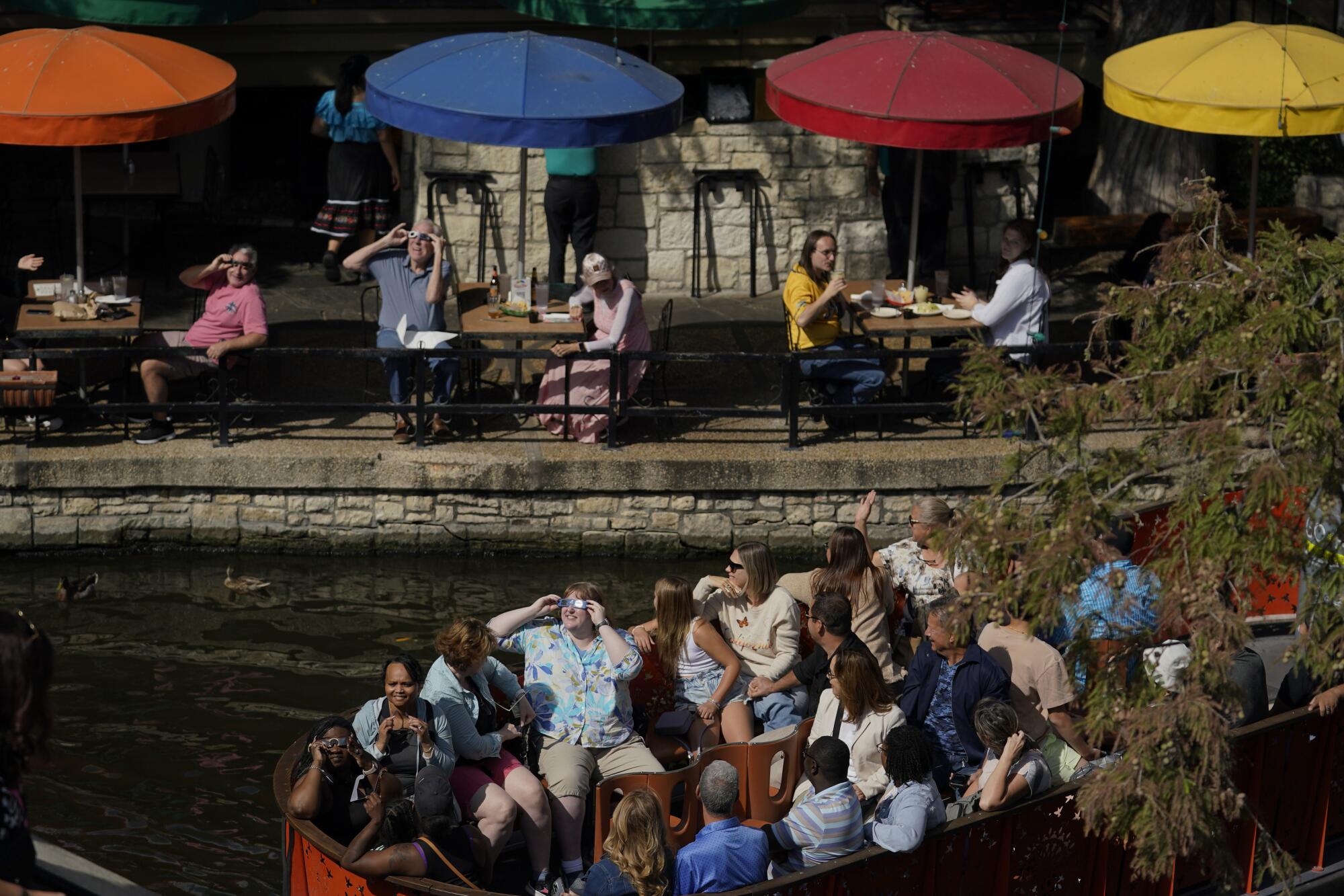 Seated diners and people nearby on a river barge in San Antonio use special glasses to watch the eclipse.