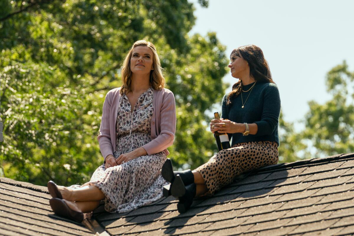 Two women sit on top of a roof on a sunny day.