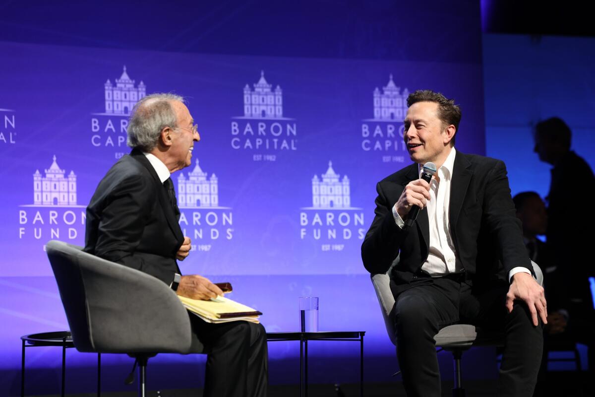 Elon Musk sits for an interview in front of the Baron Capital logo.
