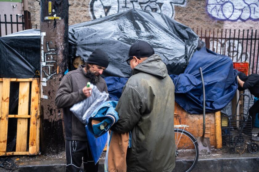 Los Angeles, CA - February 24: Volunteer with Pauly's Project Hengel Bonilla, right, 53, of Lakewood hands Javier Contreras, left, a warm jacket on Friday, Feb. 24, 2023, in Los Angeles, CA. Volunteers from Pauly's Project hand out jackets tarps, beanies, gloves, ponchos, socks, and underwear. (Francine Orr / Los Angeles Times)