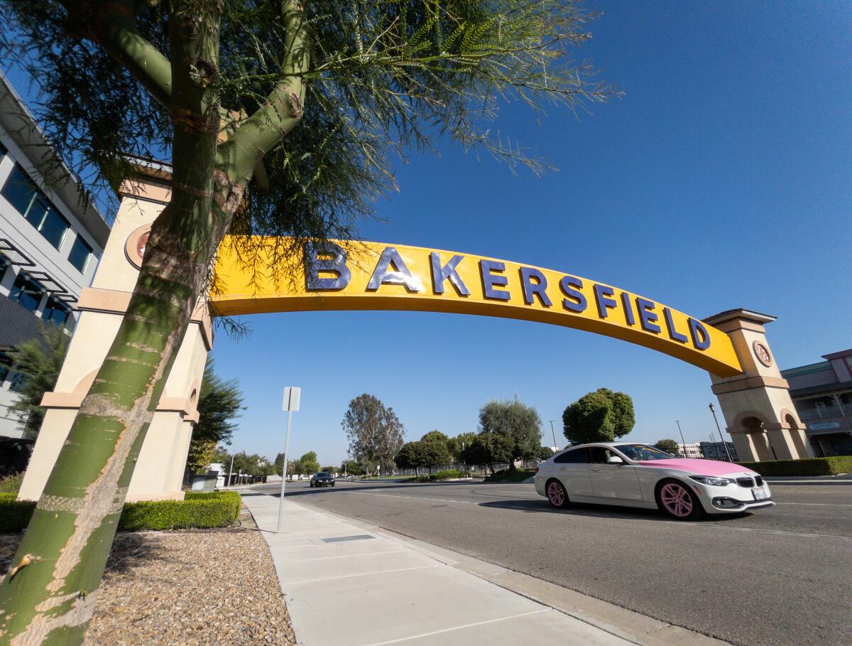 A car passing under yellow arch reading "Bakersfield" against a bright-blue sky