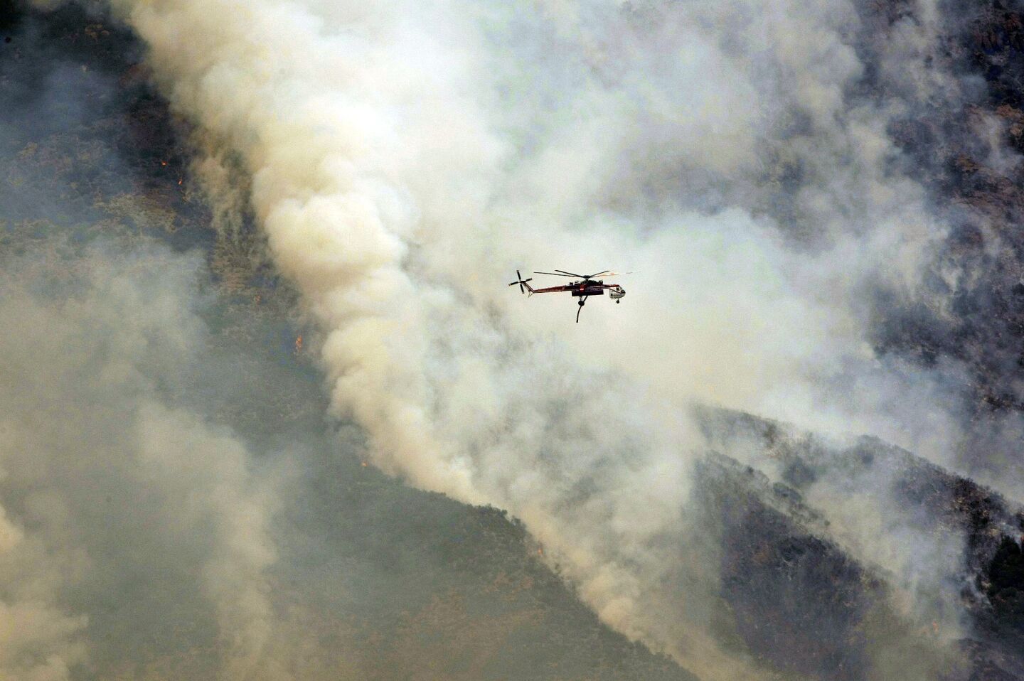 A firefighting helicopter is dwarfed by smoke and ash from the Springs fire in the mountains above Malibu.
