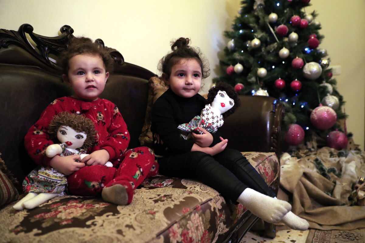Sama Chlawuit, left, and her sister Sima-Rita, whose family home had the windows blown out during August's massive explosion in Beirut, hold their dolls at their grandfather's home, in Beirut, Lebanon, Tuesday, Dec. 29, 2020. After the explosion, painter Yolande Labaki made 100 dolls for children affected by the destruction. (AP Photo/Hussein Malla)