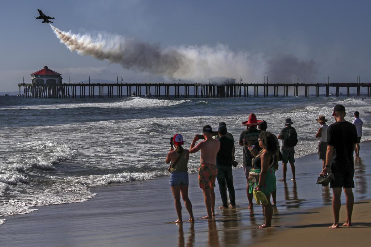 An airplane leaves a smoky trail as it performs while people watch from the beach.