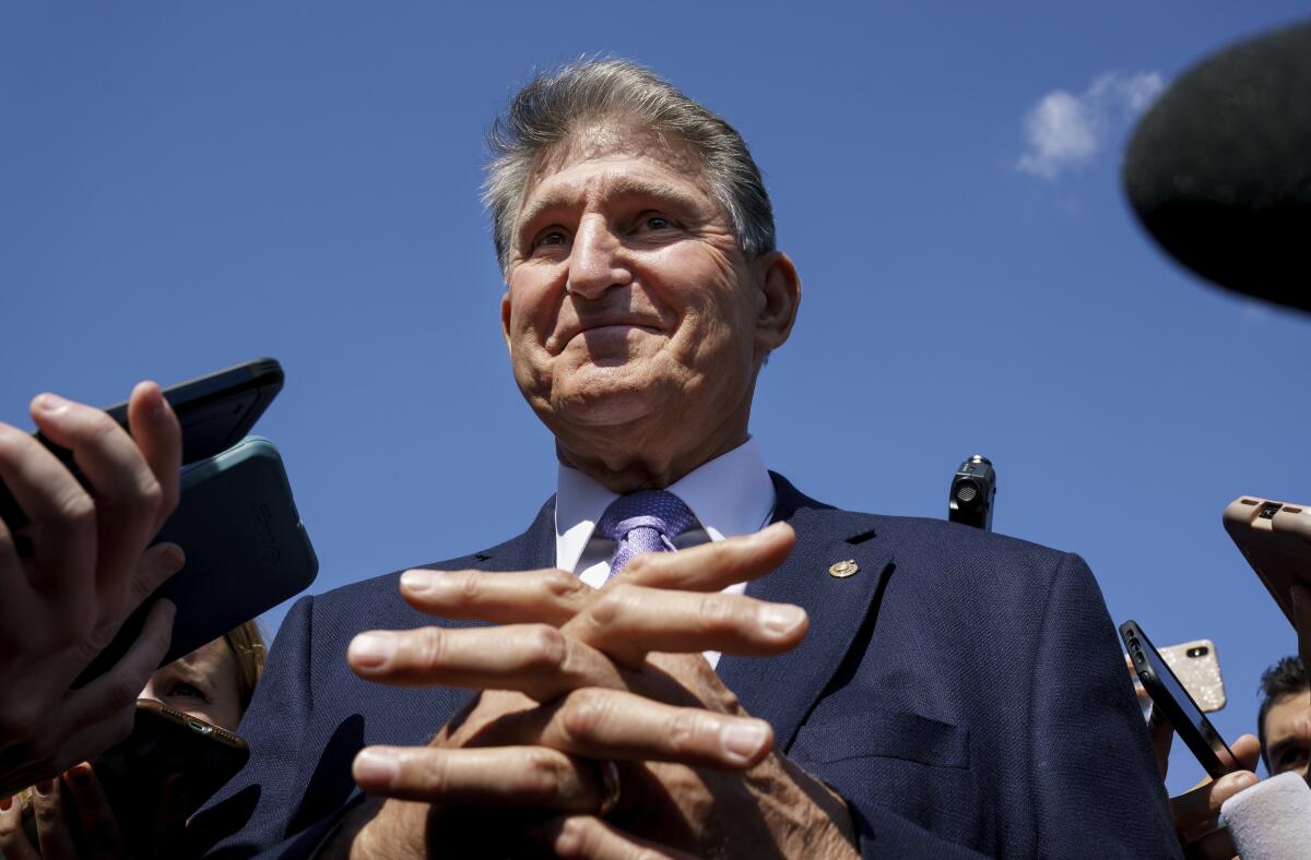 Closeup of a smiling man with his hands clasped in front of him, surrounded by smartphones held out by off-camera journalists