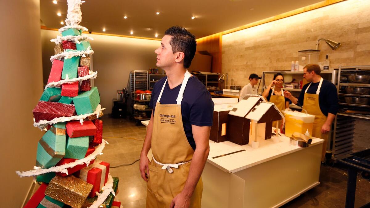Christophe Rull, executive pastry chef at Park Hyatt Aviara Resort in Carlsbad, looks at a fondant and royal icing Christmas tree, while his collaborators Liz Marek, center, and Mike Brown, right, work behind him on a giant gingerbread village.