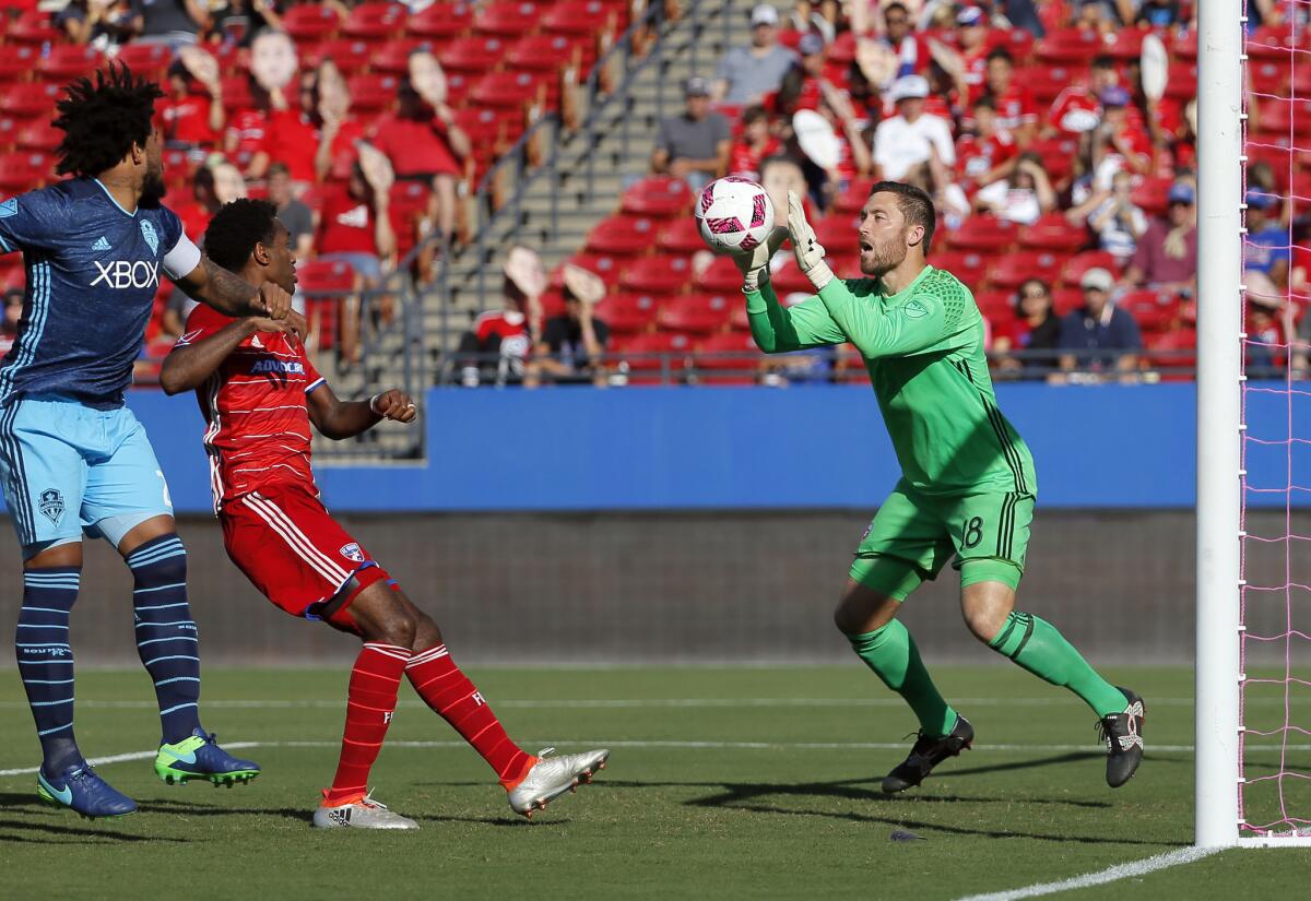 FC Dallas goalkeeper Chris Seitz (18) reaches out to make a save on a shot as Seattle Sounders defender Roman Torres, left, and Kellyn Acosta, center, watch during an MLS match on Oct. 16.
