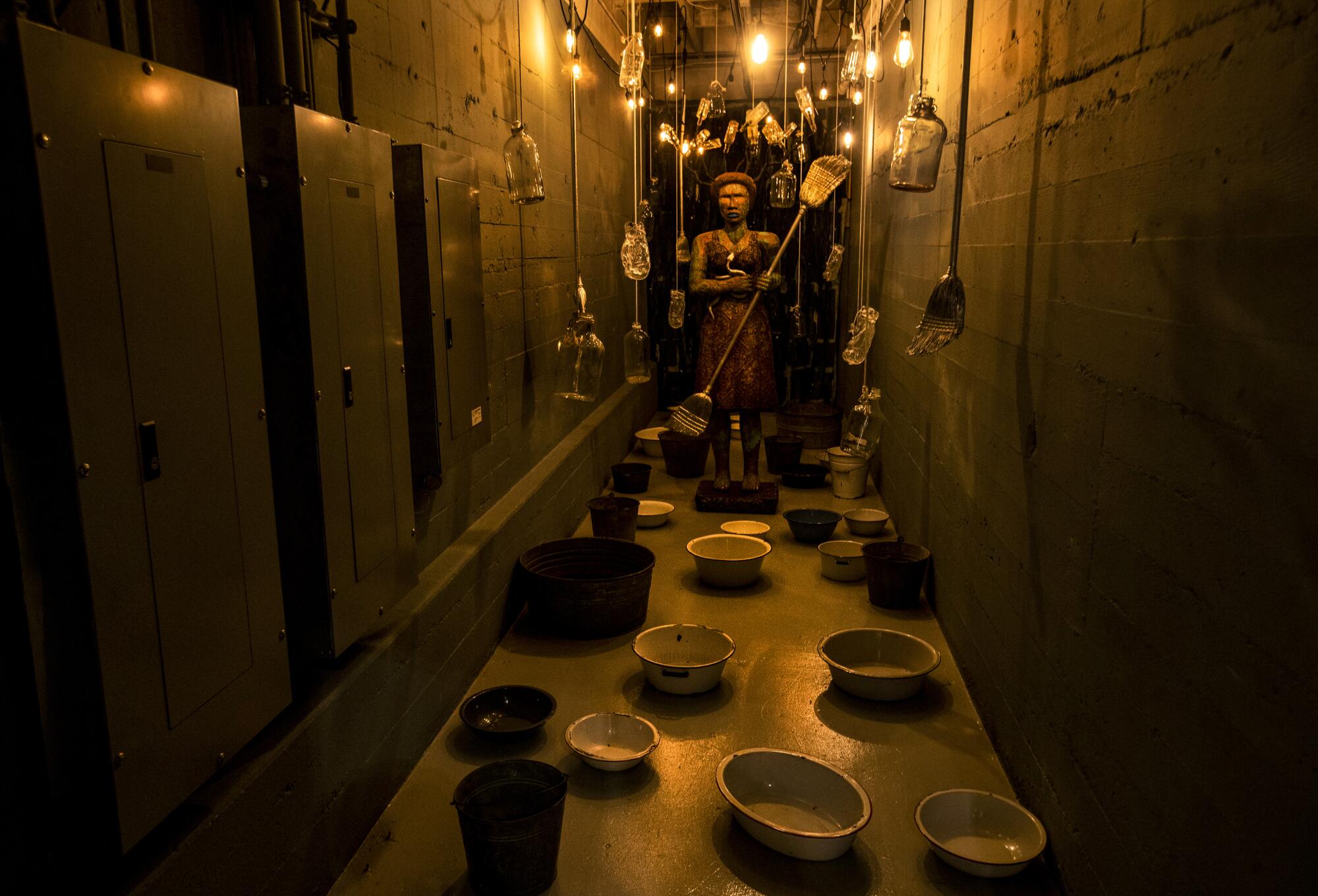 Alison Saar transforms a hallway into scene showing a woman amid washtubs and glowing lights. 