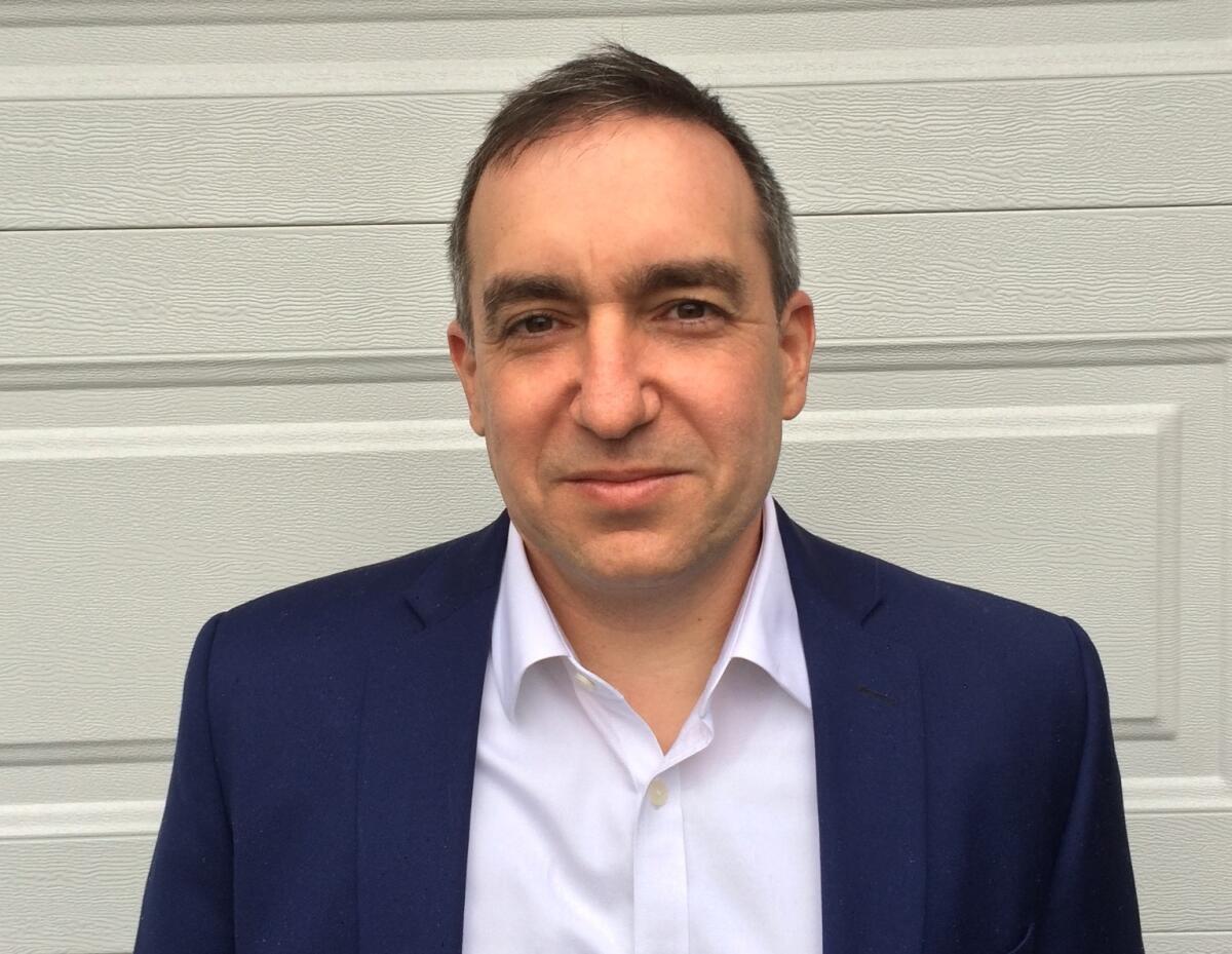 A man in a sport coat and button-down shirt in front of a door 