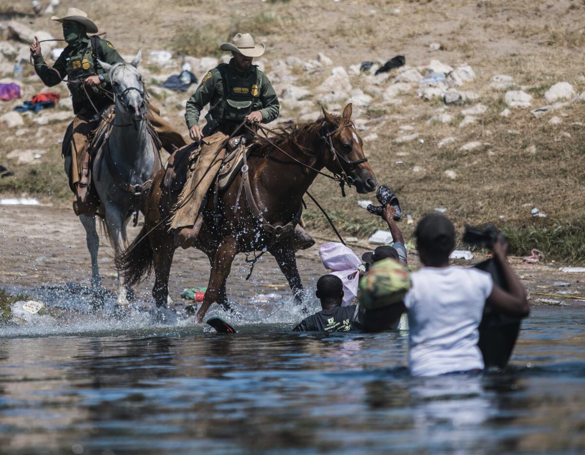 U.S. Customs and Border Protection officers on horseback block people standing in the Rio Grande.