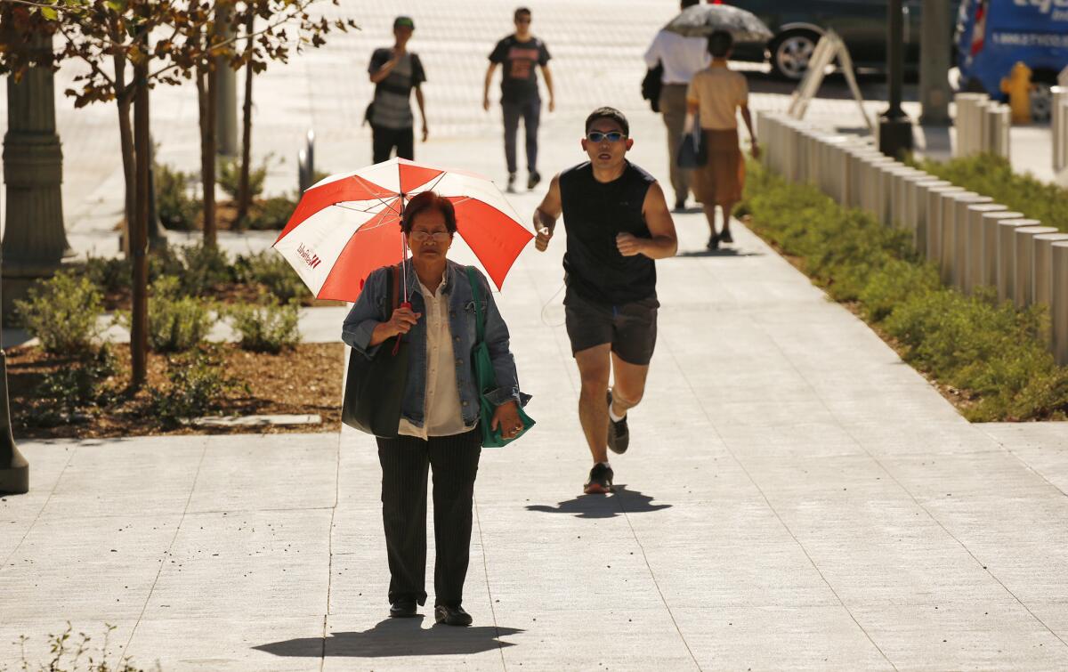 Celia Alfonso uses her red and white umbrella to shade from the sun walking in downtown Los Angeles on Sept. 26. Another red flag warning has been issued until Saturday afternoon.