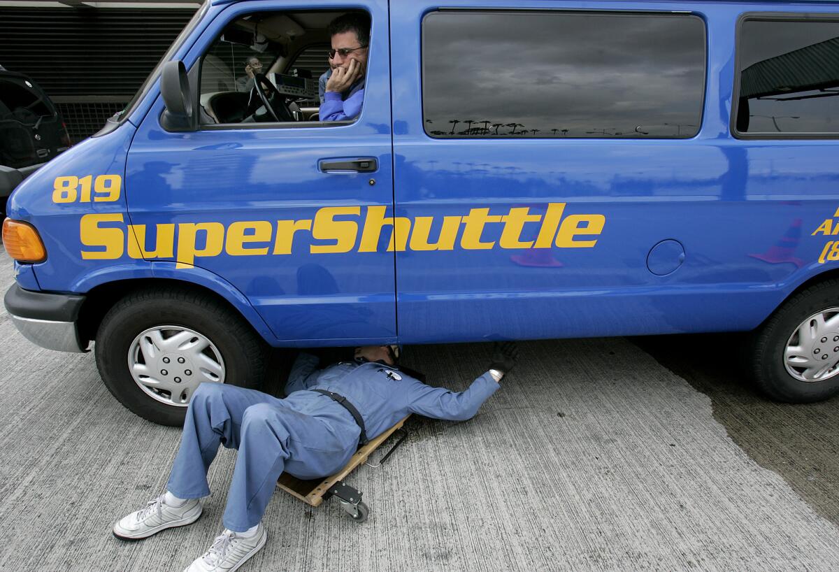 CHP motor carrier specialist Jerry Klein inspects the underbody of Vrej Tachjian's Super Shuttle van.