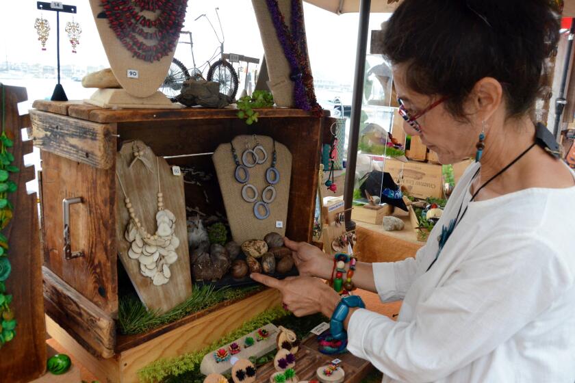 Artist Sandra Lopez shows tagua nut in original form prior to becoming an organic necklace, center left display during the Balboa Island Artwalk held Sunday. Susan Hoffman.