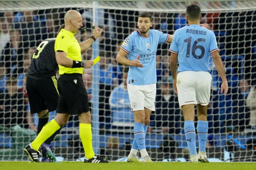 Referee Szymon Marciniak shows a yellow card to Manchester City's Ruben Dias, center, during the Champions League semifinal second leg soccer match between Manchester City and Real Madrid at Etihad stadium in Manchester, England, Wednesday, May 17, 2023. (AP Photo/Jon Super)