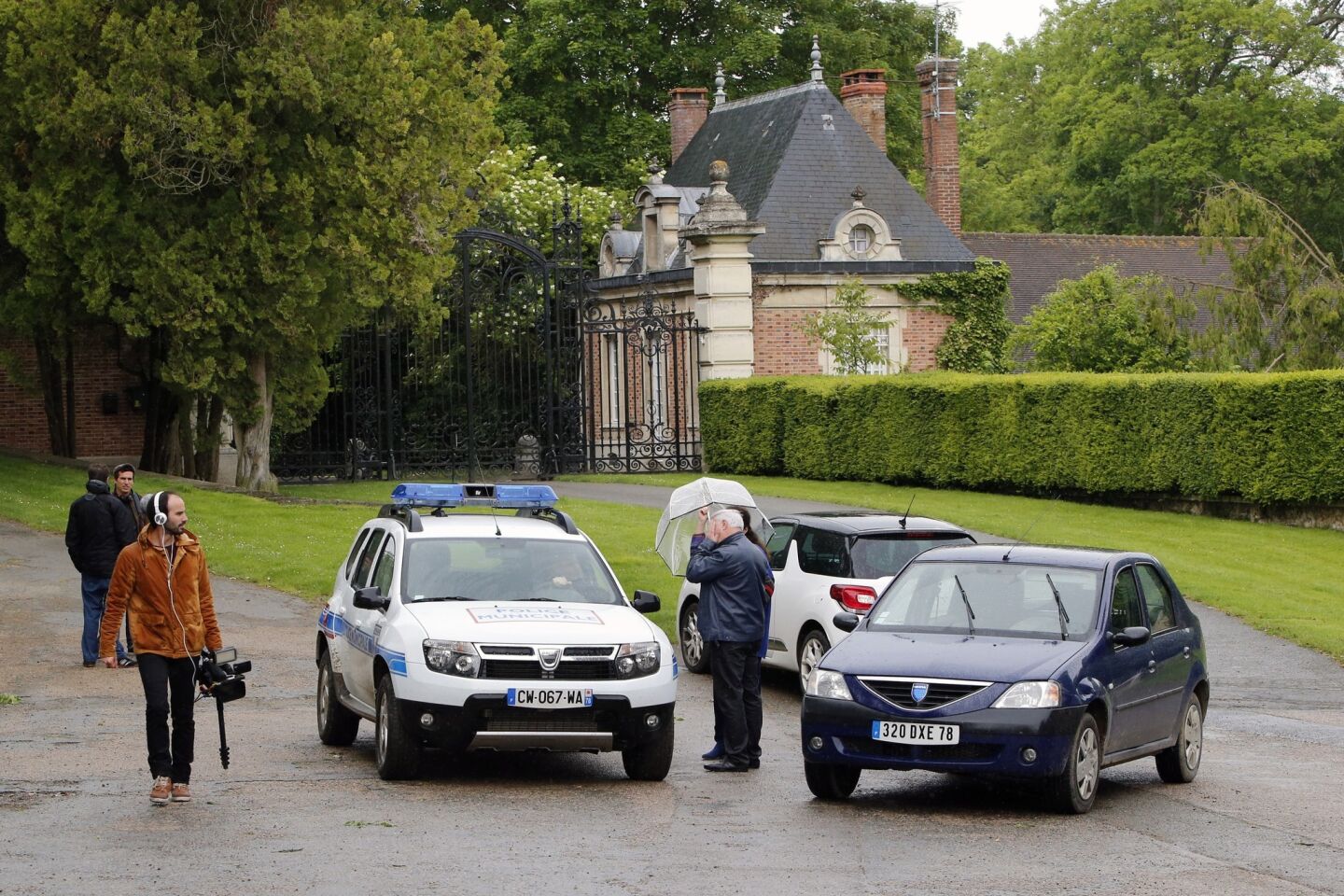A police car, onlookers and the media gather in front of the entrance of fashion designer Valentino's Chateau de Wideville, 35 miles west of Paris, where Kim Kardashian and Kanye West were expected for a brunch on May 23.