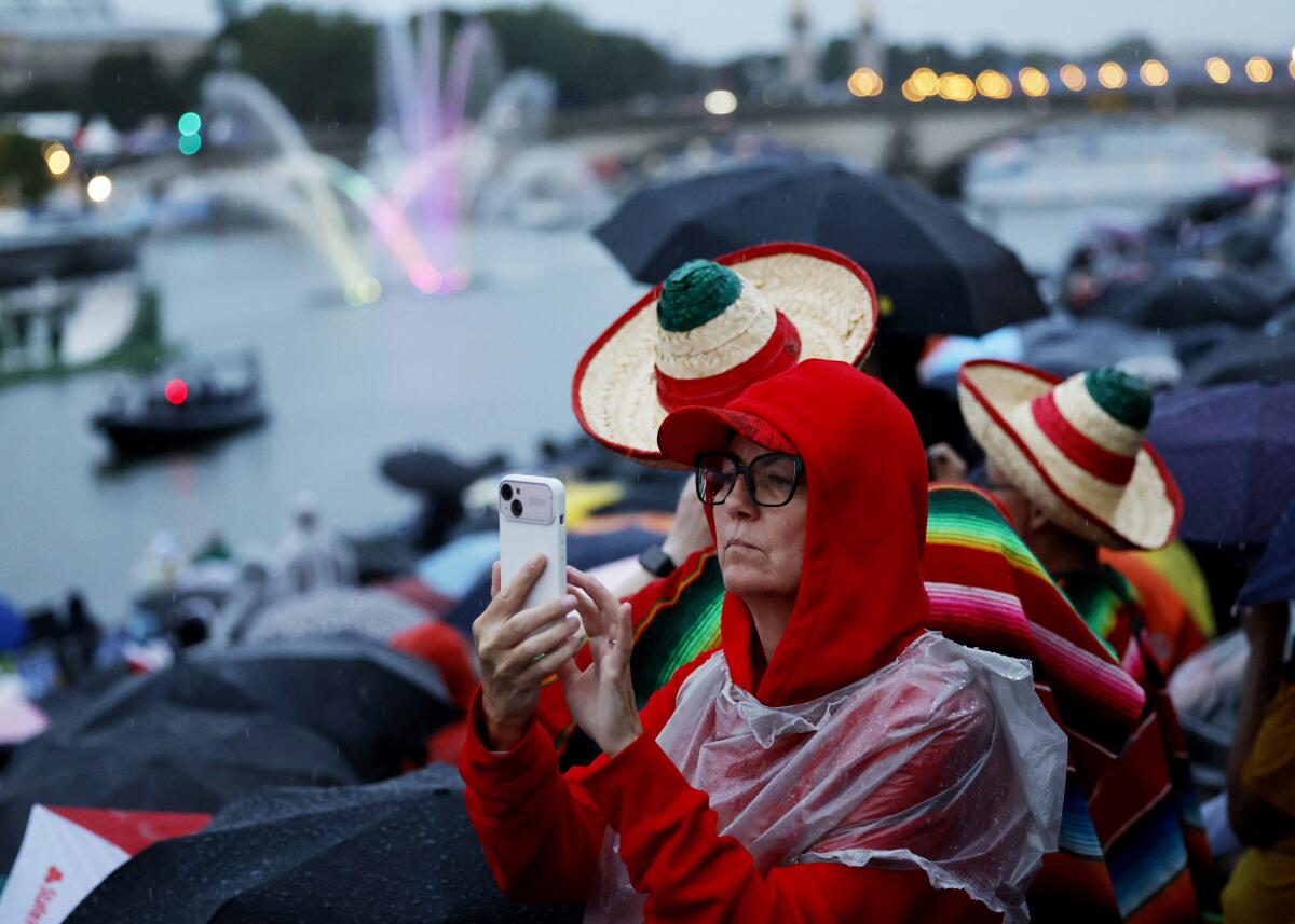 Una espectadora toma una foto con su celular mientras los deportistas pasan en barcos por el río Sena 
